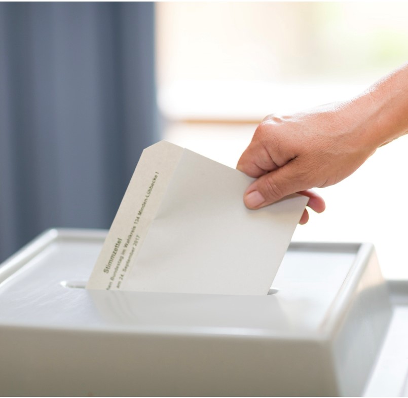 In Wahlurne wird ein Briefwahlschein eingesteckt 