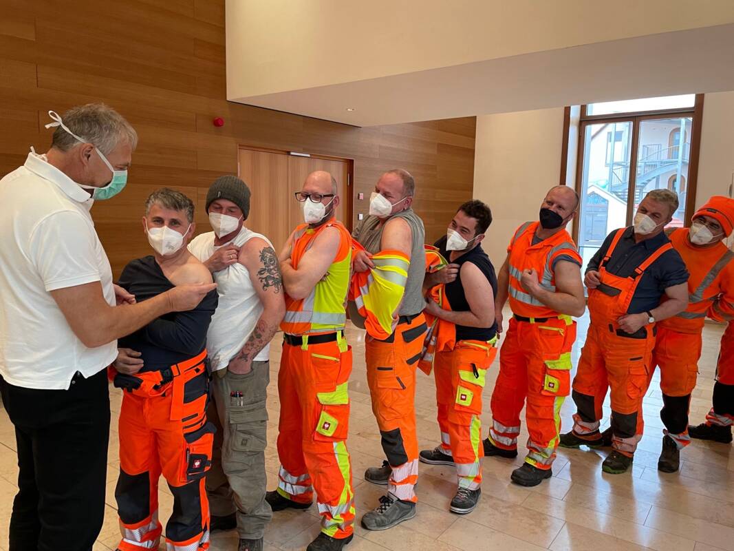 Ein humoriges Bild: Die starke Truppe des Feldkirchner Bauhofs lässt sich in der Corona-Pandemie vom Betriebsarzt impfen. 